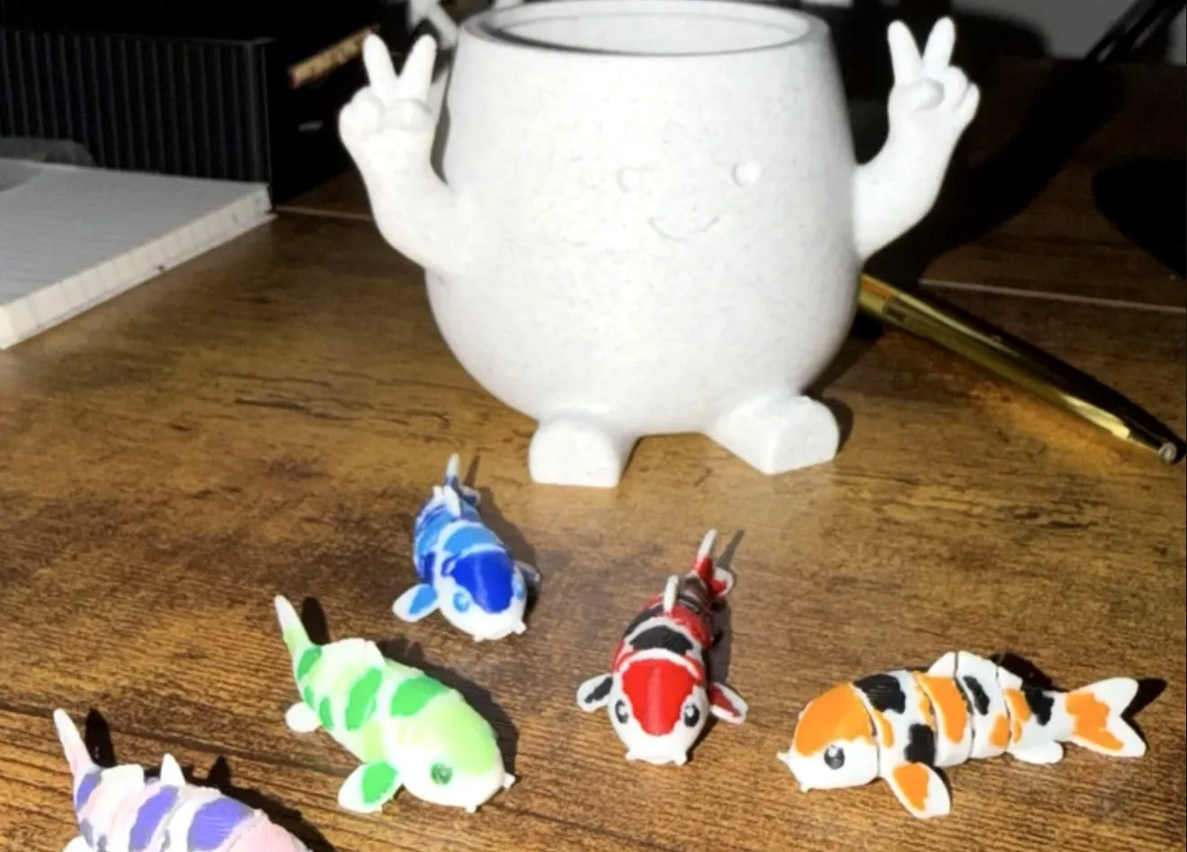 Koi articulados multicolor y una maceta blanca con forma de personaje haciendo la señal de paz
