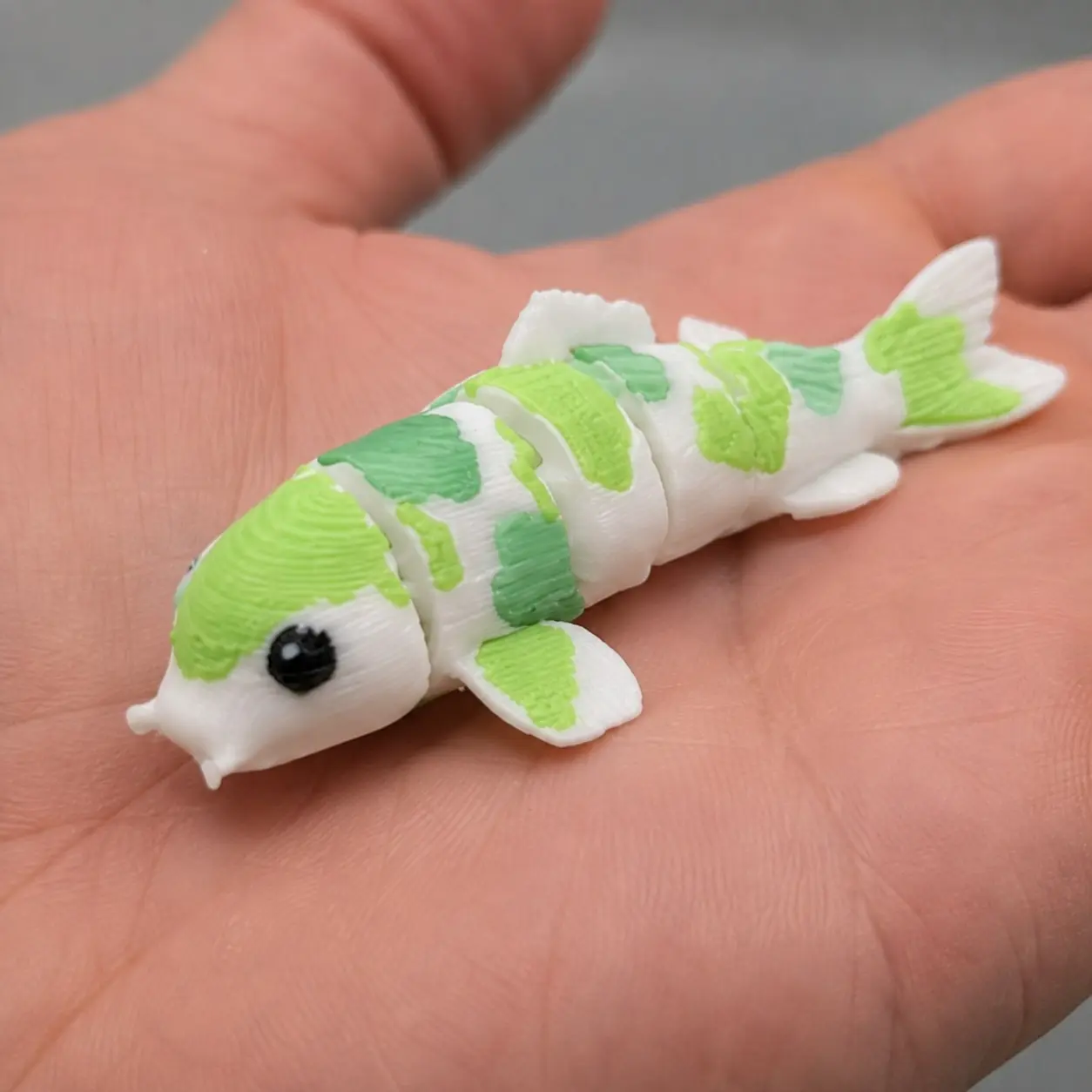 Detalle de una muestra física de koi articulado blanco y verde sostenido en una mano